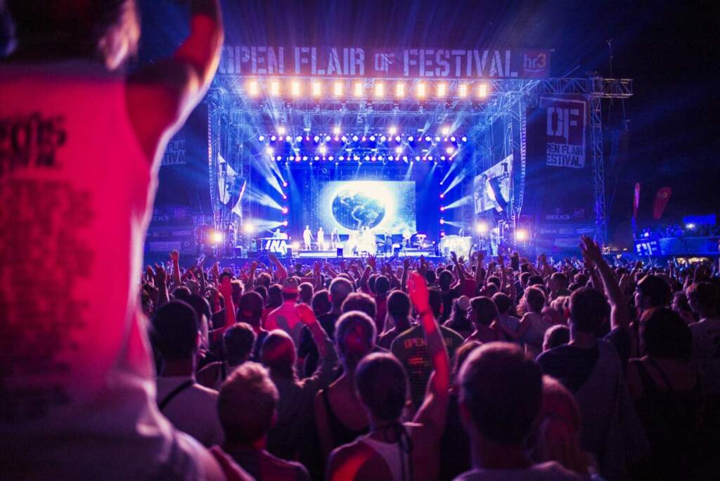 In Blau und Rot getauchte Aufnahme von Bühne des Open Flair Festivals, fotografiert über die Köpfe Huntereder Besucher, Festival Packliste, Open Air, Tipps, Downloaden, Online ausfüllen Tipps für das nächste Festival - dazu gehört auch die richtige Festival-Packliste - ZB für das extrem beliebte Open Flair Festival | (c) Paul Ripke