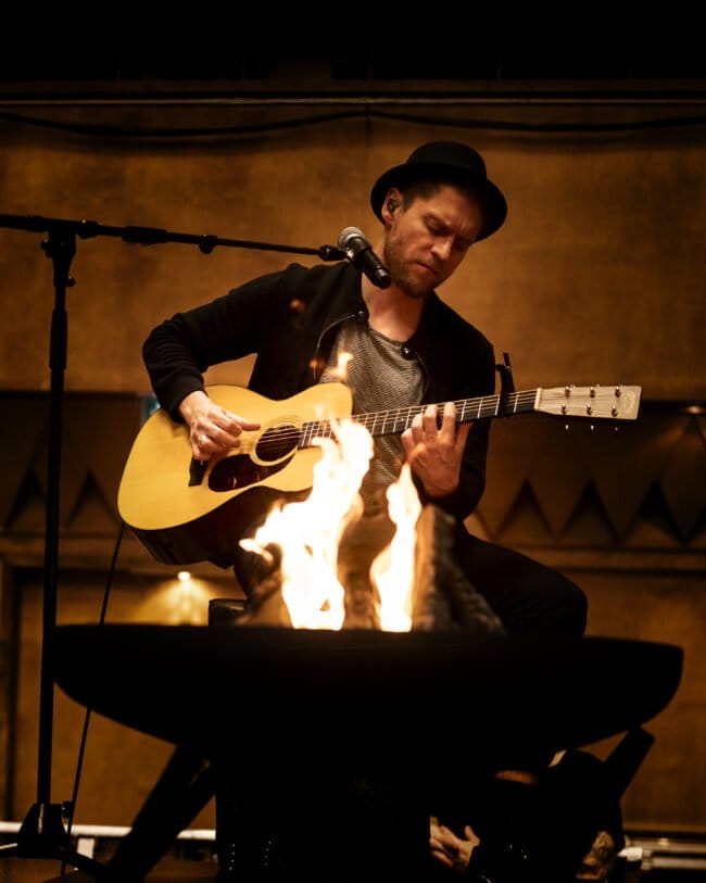 Musiker spielt Gitarre am Mikrofon vor offener Feuerschale, Johannes Oerding, Gießen Johannes Oerding bringt sanfte Töne und Lagerfeuer-Atmosphäre nach Gießen. | (c) Andreas Oetker-Kast