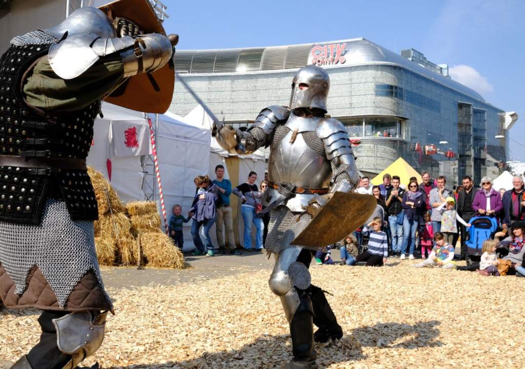 Ritter in Rüstung kämpfen bei Mittelaltershow vor Publikum, Casseler Frühlings Freyheit, Casseler Freyheit, Kassel, Mittelalter, Innenstadt, Karussell^, Königsplatz, Mittelaltermarkt, Volksfest, Jahrmarkt, Programm, Opernplatz, Flohmarkt, Auto-Mobil-Ausstellung, Familienkirmes, Verkaufsoffener Sonntag Casseler Frühlings Freyheit: Vor fast 700 Jahren rief Landgraf Heinrich der Eiserne die "Casseler Freyheit" aus. Damit begründete er eine Tradition, die bis heute in Kassel gefeiert wird - und das jetzt sogar zweimal im Jahr: Die Casseler Frühlings-Freyheit bietet viele Attraktionen und ein vielfältiges Programm, vom mittelalterlichen Spektakel auf dem Königsplatz, dem Flohmarkt mit Herz und der Familienkirmes am Friedrichsplatz bis hin zu Aktionen in der Wilhelmsstraße. Gekrönt wird das fröhliche Familienwochenende in der Kasseler City traditionell vom verkaufsoffenen Sonntag, zu dem die Händler der Innenstadt einladen.