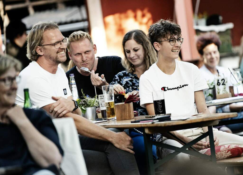 Vier Personen sitzen am Tisch und essen/trinken was, während dessen schauen sie nach vorne und lachen, , 1. Komische SommerNacht Paderborn 1. Komische SommerNacht Paderborn: Ein Sommerabend voller Humor (c) Steffi Behrmann