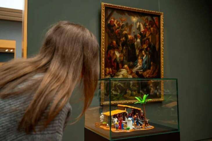 Eine Frau betrachtet eine Miniatur-Krippenszene in einem Glaskasten, während im Hintergrund ein klassisches Gemälde mit einer ähnlichen Darstellung an der Wand hängt. Kasseler Museums Nacht - PLAYMOBIL trifft Gemäldegalerie – Alte Meister neu erzählt | (c) Hessen Kassel Heritage - Bernd Schoelzchen