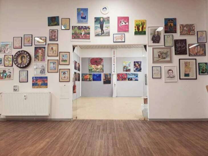 Ein Ausstellungsraum mit Wänden, die dicht mit verschiedenen Gemälden und Zeichnungen in unterschiedlichen Rahmen behängt sind, bietet einen Blick auf weitere Kunstwerke im Hintergrund. Kasseler Museums Nacht - work in process – Ausstellungsperformance | (c) Galerie in Amos