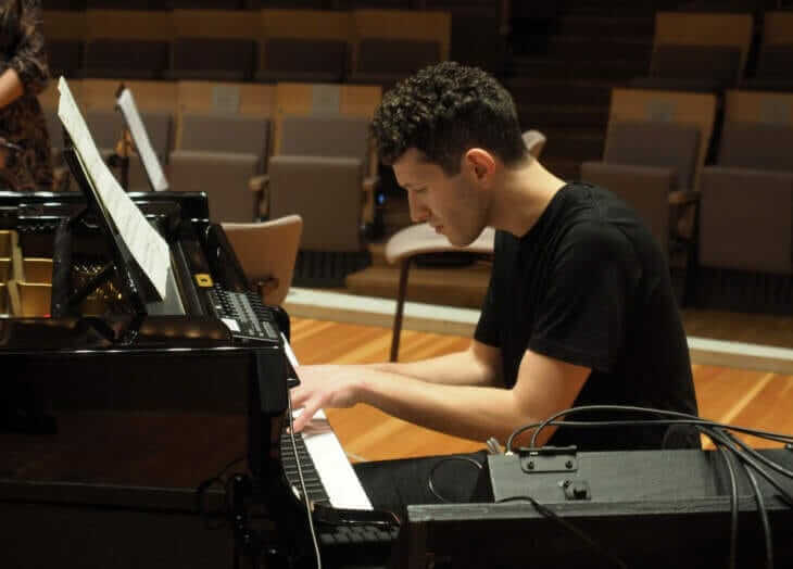 Kaan Bulak spielt konzentriert Klavier auf einer Bühne, mit Notenblatt vor sich und leeren Sitzreihen im Hintergrund. Kaan Bulak | Kasseler Musiktage 2024 | (c) do Siegfriedt