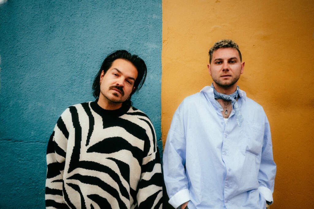 Zwei Männer vor blauer und gelber Wand, Milky Chance vor zweifarbiger Wand: Stilvolles Duo als Vorschau auf das Konzert in der Karlsaue mit dem Kasseler Staatsorchester. Seit der Gründung im Jahr 2012 hat Milky Chance den Sprung aus Kassel auf die internationalen Bühnen geschafft. | Anthony Molina