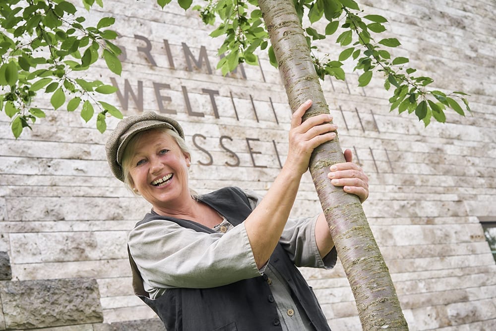 Märchenerzählerin Andrea C. Ortolano steht vor der GRIMMWELT Kassel. Sie trägt eine Schiebermütze und lächelt in die Kamera. Märchenerzählerin Andrea C. Ortolano | (c) GRIMMWELT Nikolaus Frank
