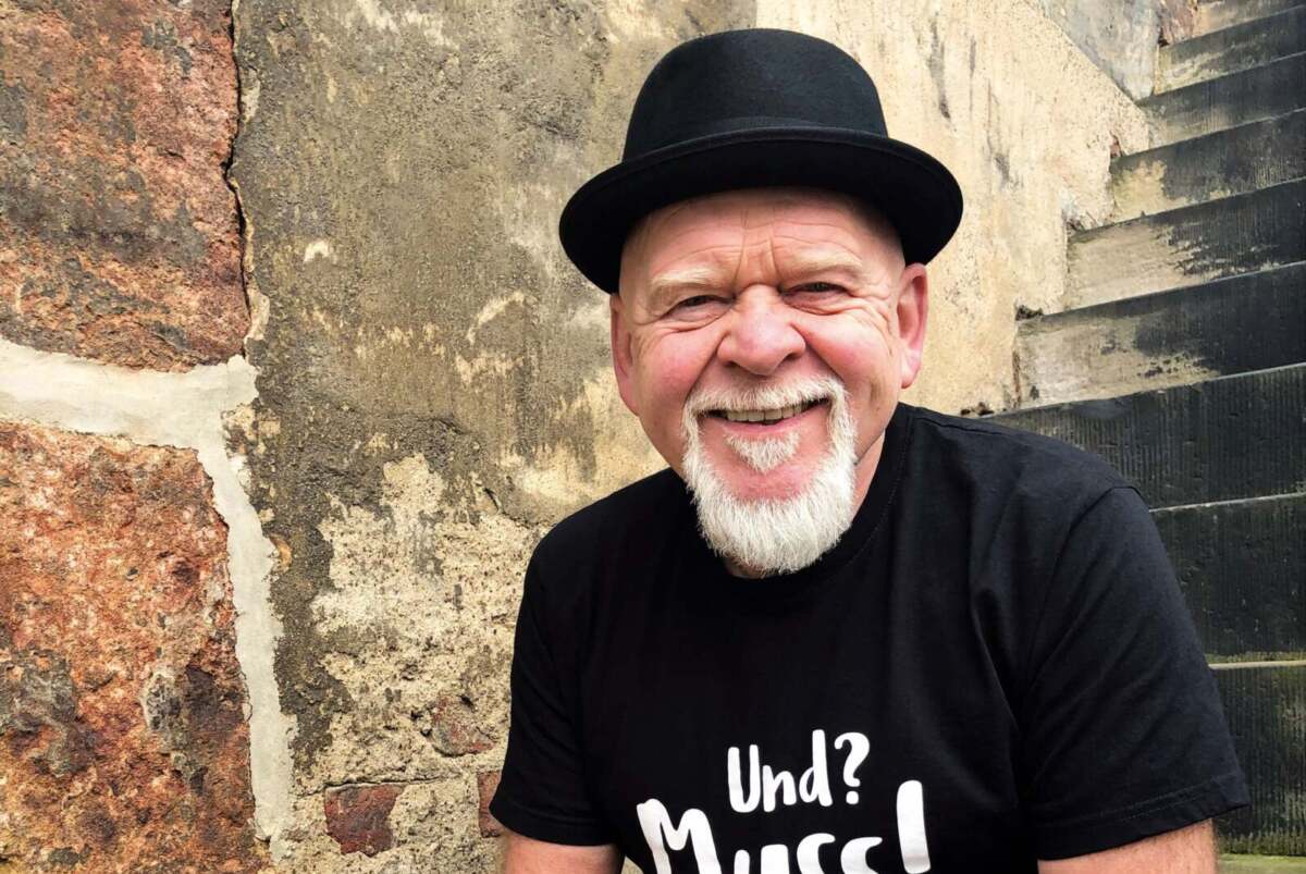 Bernd Gieseking sitz in Jeans und T-shirt auf den Stufen zum mittelalterlichen alten Warburger Rathaus. Bernd Gieseking - Treppe Warburg Altes Rathaus - (c) Martina Lorenz