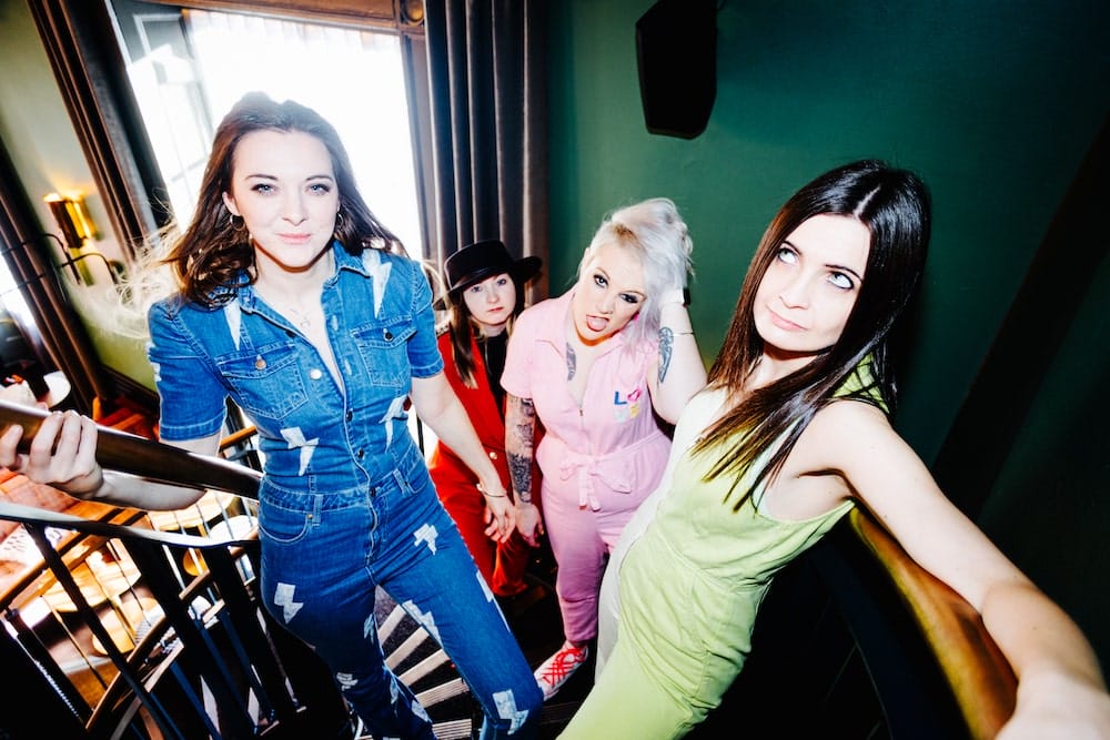 Vier Frauen der Band „The Hot Damn!“ in bunten Outfits auf einer Treppe, Thoe Hot Damn!, Schwalmtal Direkt aus England nach Schwalmtal: The Hot Damn! performt auch in Nordhessen. | (c) The Hot Damn!