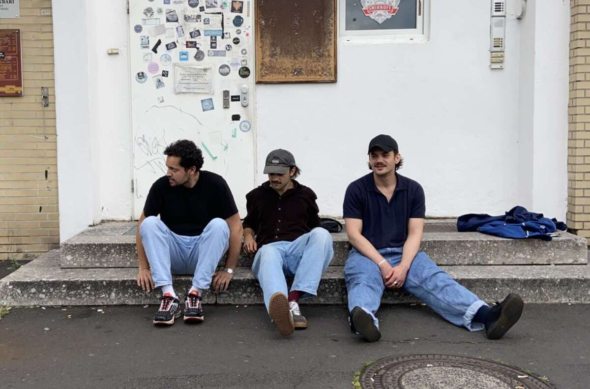 Drei Bandmitglieder sitzen locker auf Betontreppe vor Wand. TDie Band There, There beim StäPs-Festival in Marburg: Das Alternative-Trio aus Köln steht für ständige stilistische Wandlung – mit Anklängen an Radiohead, Tame Impala und Deftones bringen sie live eine eindrucksvolle Klanggewalt auf die Bühne. | (c) There, There