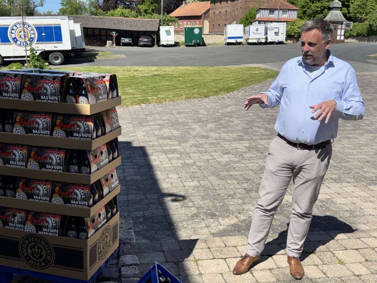 Mann erklärt Warburger Dunkel alkoholfrei neben Bierkisten draußen Franz-Axel Kohlschein, einer der Inhaber der Warburger Brauerei Kohlschein erläutern das Konzept des neuen Displays der Warburger Brauerei. Hier bestückt mit dem neuen Bier Warburger Dunkel Alkoholfrei | (c) Fedor Waldschmidt