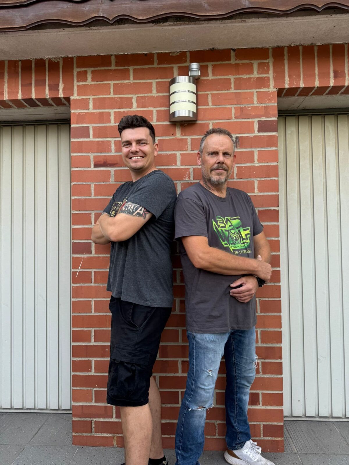 Die beiden Rockschuppen Treysa stehen vor einer Steinwand und lächeln den Betrachter an, tragen T-Shirt und Jeans ode 72r kurze Chino Die Rockschuppen Macher Marco & Jörg wollen den Spirit vom alten Laden mitnehmen!| (c) Marco Kohrell