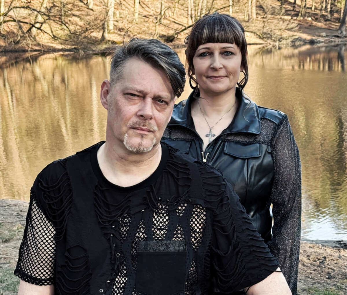 Auf dem Foto sind die beiden Mitglieder der Band My Silence Romance zu sehen. Sie tragen schwarze Kleidung mit dezenten Gothic-Elementen und stehen an einem Seeufer, vor einem ruhigen Wasser und kahlen Bäumen im Hintergrund. Zwischen See und Synths: My Silence Romance stimmen sich auf ihren Auftritt bei der Synthpop Night Vol. 1 im Knubbel Marburg ein. | (c) My Silence Romance