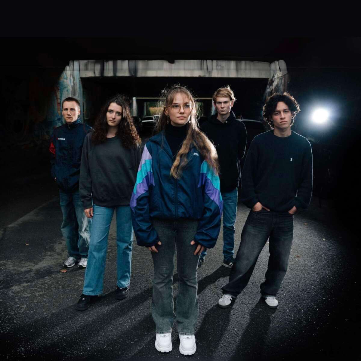 Pressebild der Indie-Band The Livelines – Fünfköpfige Gruppe mit urbanem Look in dramatischer Lichtstimmung unter einer Brücke Die junge Indie-Band The Livelines bringt frischen Wind aufs Haune Rock 2026. Mit melancholischen Melodien, klaren Texten und einem ganz eigenen Stilgefühl zeigen sie, dass ehrliche Musik keine Altersgrenze kennt – präsentiert vom Wildwechsel, der Talente fördert und feiert. | (c) Lion Schlenter