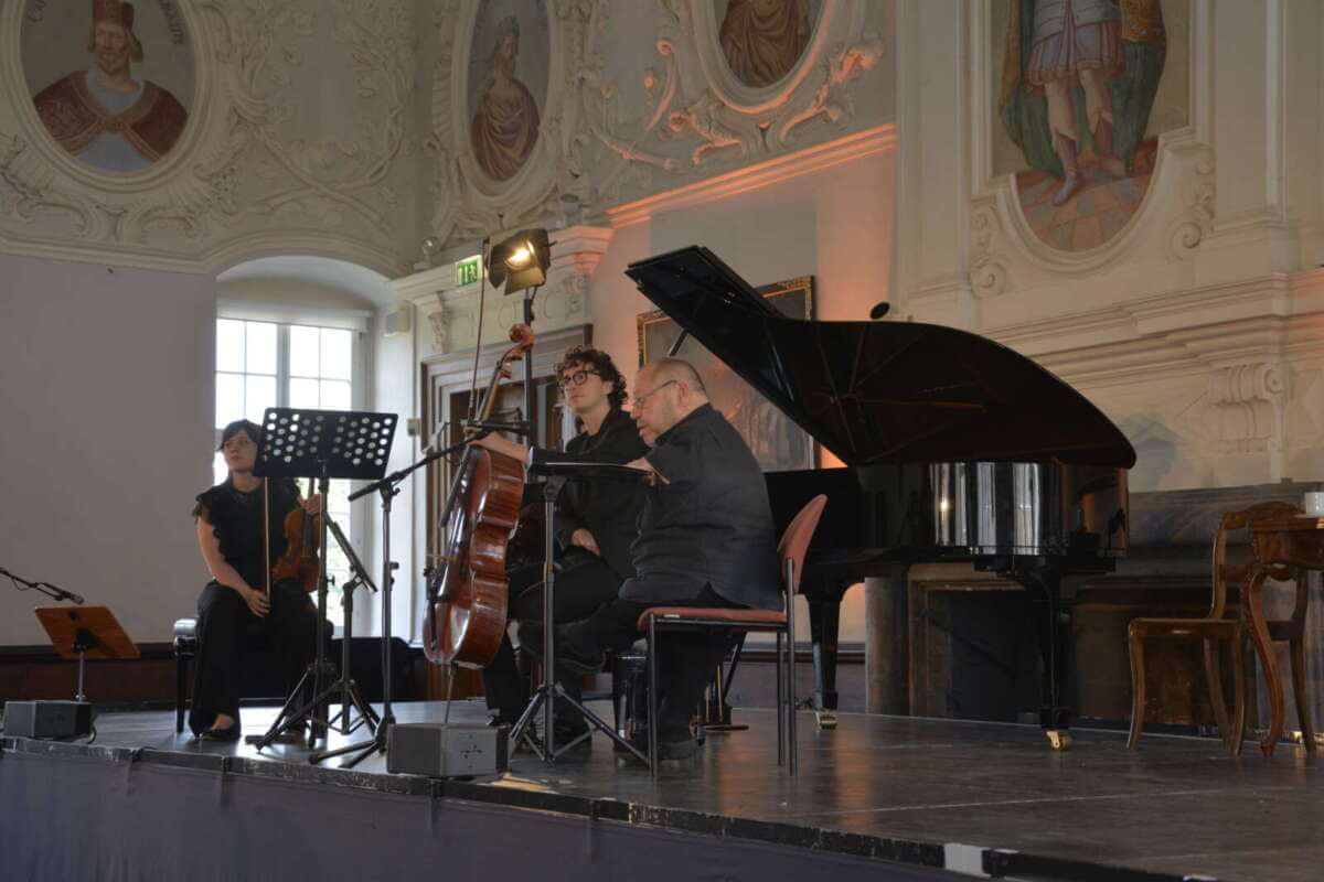 Via Nova Kunstfest 2025 im Schloss Corvey: Thomas Quasthoff und Amatis Piano Trio spielen »Menschlichkeit im Krieg«. Das Bild hält neben den Künstlern und Ihren Instrumenten einen prunkvollen Saal, mit Stuck und Gemälden fest.