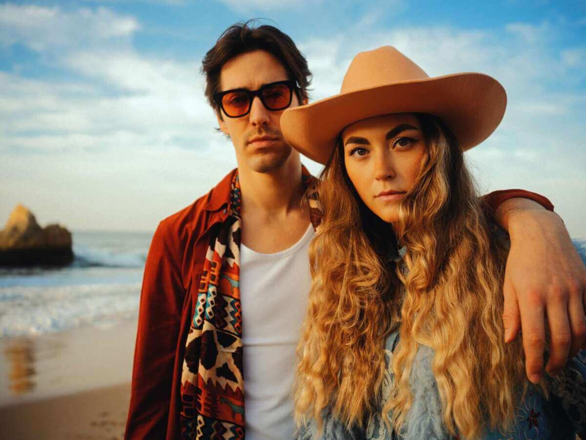 Cari Cari stehen eng am Strand, Meer und Felsen im Hintergrund, warmes Abendlicht. Cari Cari bringen ihren lässigen Indie-Sound ins Kulturzelt Kassel 2026. | (c) Andreas Jakwerth