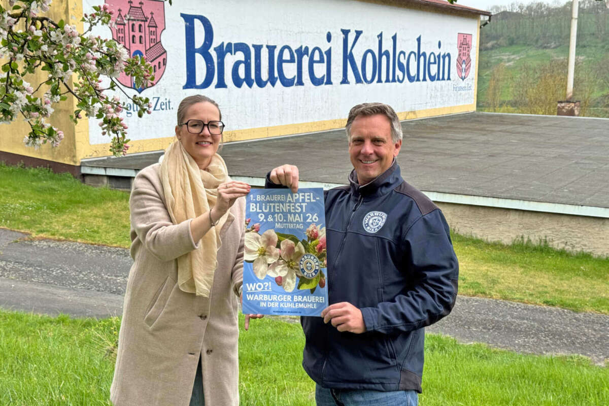 Valeria Geritzen und Franz-Axel Kohlschein stehen vor der Fassade der Brauerei Kohlschein und präsentieren ein Plakat für das „1. Brauerei Apfelblütenfest“ am 9. und 10. Mai 2026.  | (c) Wildwechsel.de
