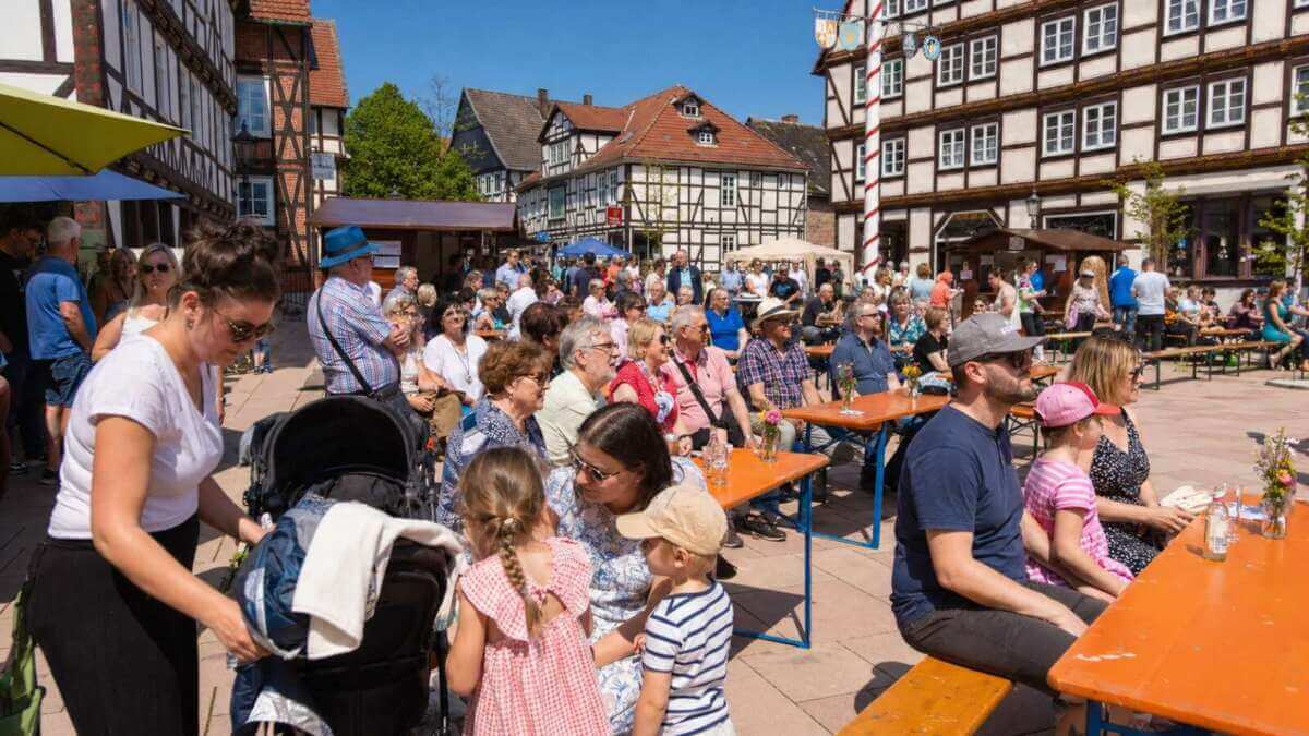 Sonnige Pausen beim Dornröschenfest Hofgeismar: Familien und Besucher genießen auf dem Marktplatz zwischen Fachwerkhäusern, Ständen und Bierbänken das entspannte Flair des beliebten Märchen- und Stadtfestes. Dornröschenfest Hofgeismar - KI generiert - (c) Wildwechsel