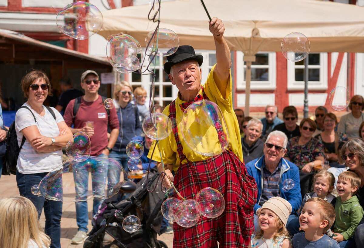 Ein Straßenkünstler begeistert beim Dornröschenfest Hofgeismar mit schillernden Seifenblasen Groß und Klein – mitten im bunten Treiben der Altstadt wird das märchenhafte Stadtfest zum lebendigen Erlebnis für die ganze Familie. Dornröschenfest Hofgeismar - KI generiert - (c) Wildwechsel