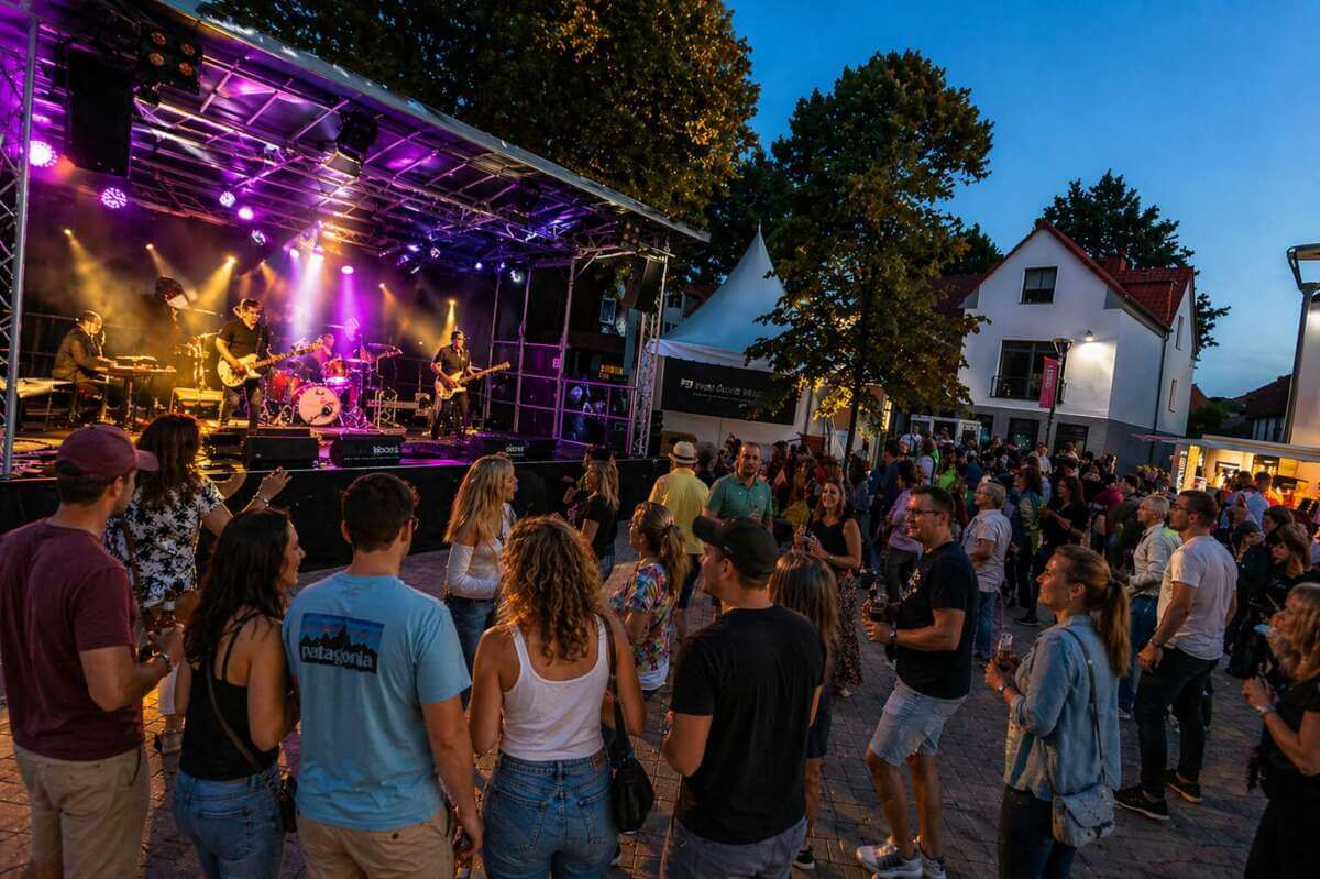 Live-Musik unter freiem Himmel erwartet die Besucher beim Stadtfest Brakel 2026: Eine Band sorgt auf der Bühne für Festivalstimmung, während Besucher dicht gedrängt vor der Bühne tanzen, feiern und den Sommerabend genießen. | Ki-generiert - (c) Wildwechsel.de