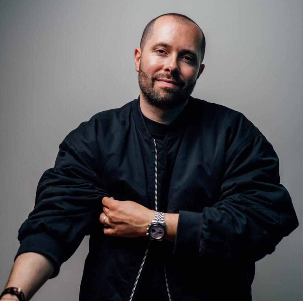 David Puentez sitzt vor einem hellgrauen Hintergrund und schaut freundlich in die Kamera. Er trägt eine schwarze Jacke und eine auffällige Uhr, passend zum modernen House- und EDM-Programm des Lippe Open Air 2026. DaDavid Puentez im schwarzen Outfit, DJ im Lippe Open Air 2026 Line-Up. | (c) FABS Foundation