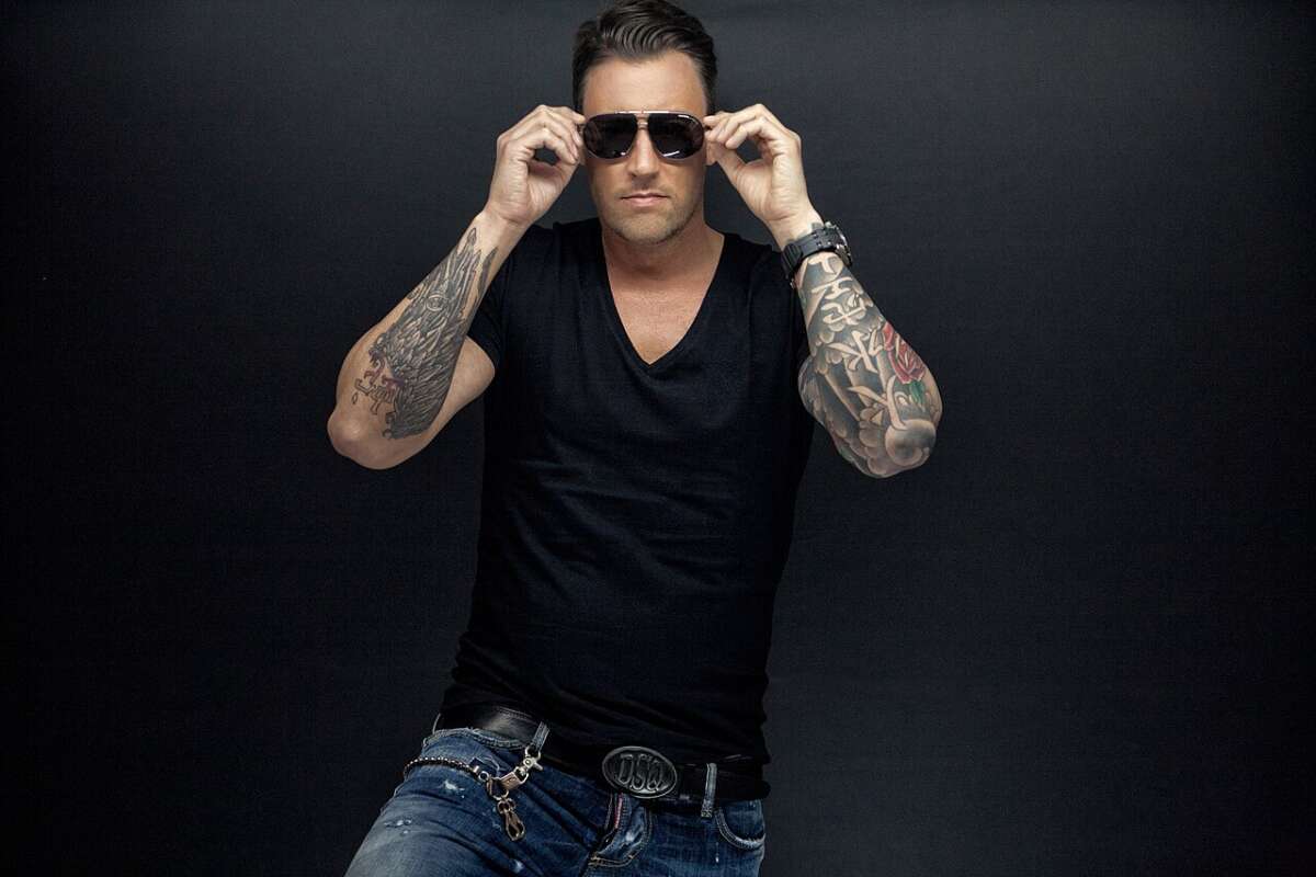 Das Studiofoto zeigt Niels Van Gogh frontal vor dunkler Kulisse. Sonnenbrille, Tattoos und schwarze Kleidung geben dem Motiv einen klaren Club-Look, der die elektronische Seite des Lippe Open Air 2026 betont. Niels Van Gogh mit Sonnenbrille und Tattoos, DJ-Act beim Lippe Open Air 2026. | (c) Niels van Gogh