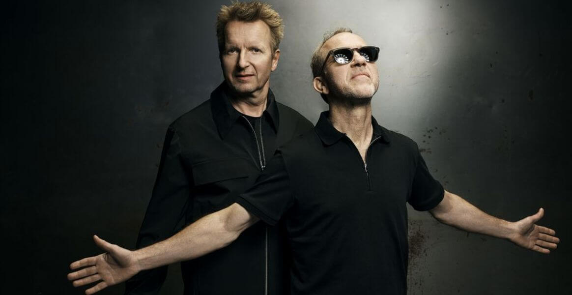 Das Bild zeigt Safri Duo in schwarzer Kleidung vor grauem, leicht dramatischem Hintergrund. Die offene Armhaltung und der ernste Blick unterstreichen die energiegeladene Percussion-Power im Programm des Lippe Open Air 2026. Safri Duo vor dunklem Hintergrund, Act beim Lippe Open Air 2026 in Lemgo. | (c) Robin Skjoldborg