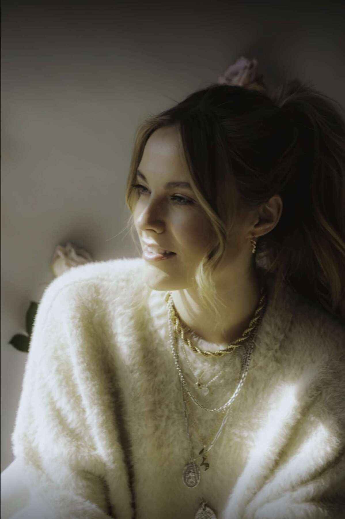 Das Bild zeigt Sophia im weichen Licht. Sie trägt einen hellen, flauschigen Pullover und Schmuck, ihr Haar ist zum Zopf gebunden, der Blick geht zur Seite. Sophia tritt beim Butzbach Open Air 2026 auf und ist auf einem stimmungsvollen Porträt in hellem Pullover zu sehen. | (c) Paul Hüttemann