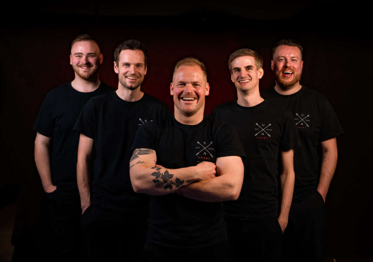 Die fünf Musiker von Unart posieren in schwarzen Shirts vor dunklem Hintergrund. Die Band gehört zum Liveprogramm der Warburger Oktoberwoche 2026 in Warburg.