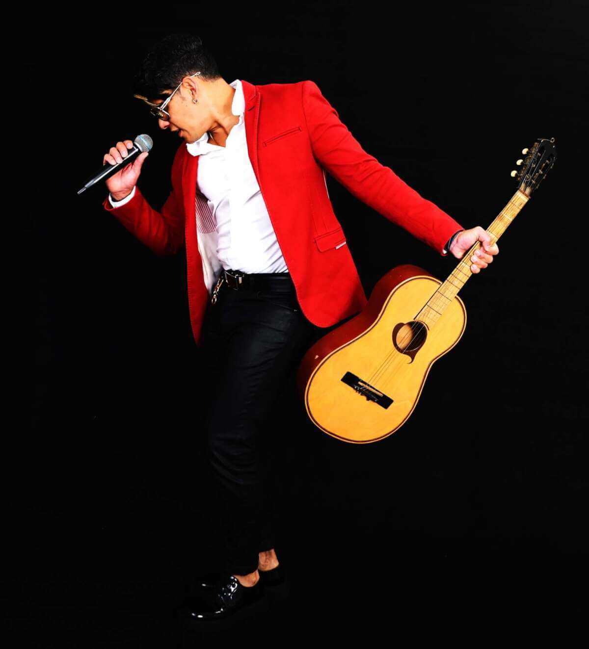 Rody Reyes mit Mikrofon und Gitarre vor schwarzem Hintergrund während eines Künstlerporträts. (c) Rody Reyes & Havanna con Klasse)
