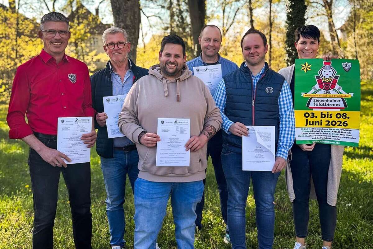 Auf einer sonnigen Grünfläche posieren Vertreterinnen und Vertreter der Stadt, des Organisationsteams und weiterer Beteiligter für ein Gruppenfoto. Mehrere Personen halten Vertragsunterlagen, während rechts im Bild ein Plakat der Ziegenhainer Salatkirmes gezeigt wird. Im Hintergrund stehen große Bäume mit frischem Laub. Die Aufnahme symbolisiert den offiziellen Start der Vorbereitungen für die kommende Salatkirmes in Schwalmstadt. Gruppenfoto zur Vertragsunterzeichnung der Ziegenhainer Salatkirmes mit Vertretern von Stadt und Veranstaltern.| (c) Stadt Schwalmstadt