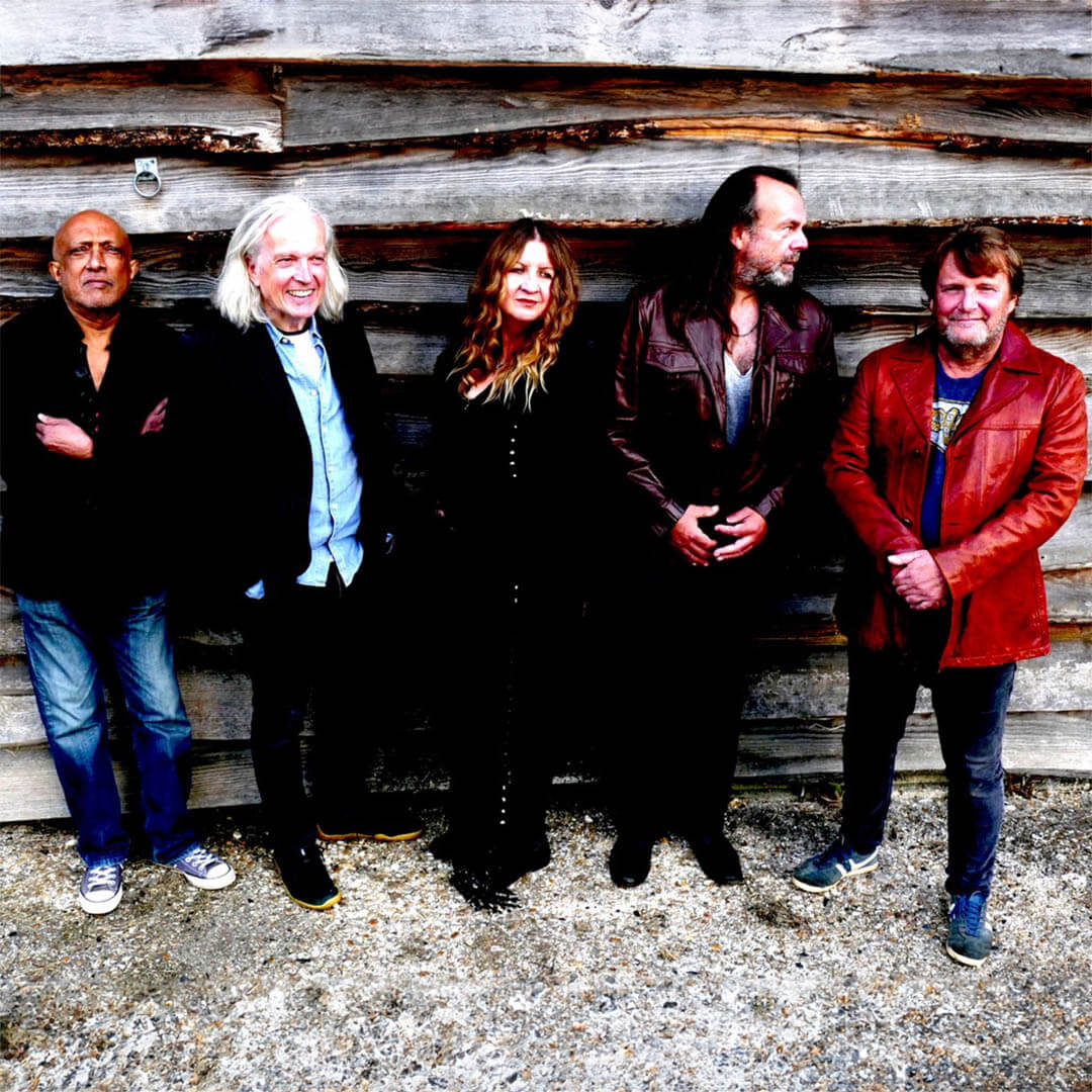 Fünfköpfige Bluesrock-Band vor einer rustikalen Holzwand, die Sängerin steht in schwarzer Kleidung in der Bildmitte. | (c) David Cunningham
