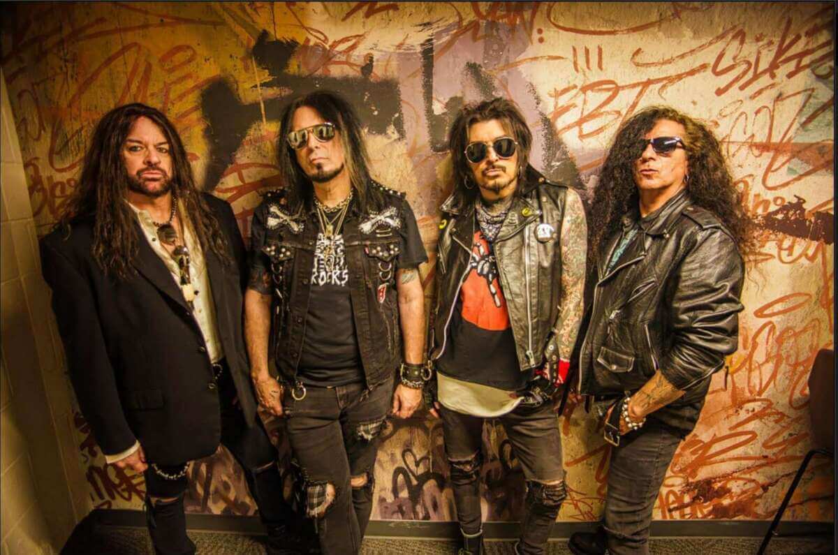Vier Männer der US-Hardrock-Band Kickin Valentina stehen dicht nebeneinander vor einer Wand mit bunten Graffiti und Schriftzügen. Sie tragen überwiegend schwarze Kleidung aus Leder und Jeans sowie Sonnenbrillen. Lange Haare, Bärte, Tattoos und rocktypische Accessoires wie Nieten und Ketten prägen ihr Erscheinungsbild. Die Band blickt ernst in die Kamera und vermittelt den Eindruck eines klassischen Hardrock- und Rock'n'Roll-Acts. Die Aufnahme wirkt warm ausgeleuchtet und unterstreicht die raue, urbane Atmosphäre des Motivs. Offizielles Pressefoto der Hardrock-Band Kickin Valentina für ihren Auftritt beim Rock N Revel 2026. | (c) Kickin Valentina