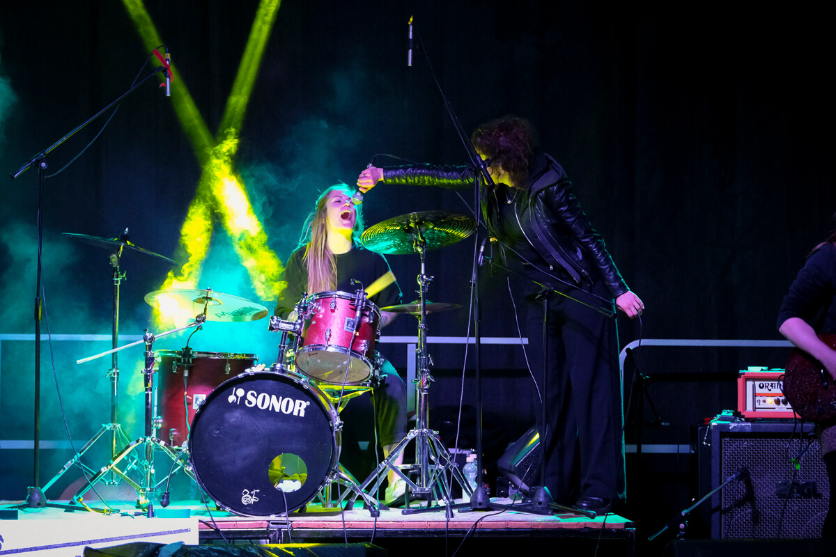 Band bei einem Live-Auftritt auf der Bühne des Kraut & Rüben Musikfestivals in Hembsen mit Schlagzeug, Gesang und farbiger Lichtshow. | (c) Ela Rüther