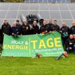 Organisationsteam der Schöninger Holz- und Energietage mit Werkzeugen und Veranstaltungsbanner vor Solarmodulen